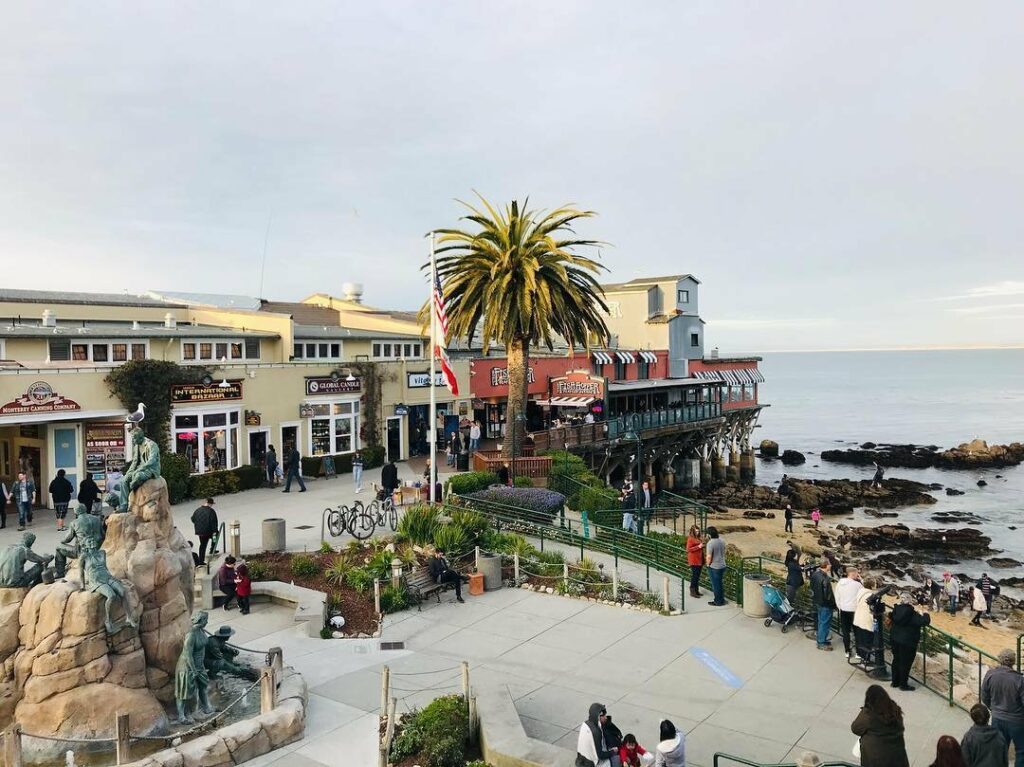 People walking around a pier and a building with a statue in Cannery Row