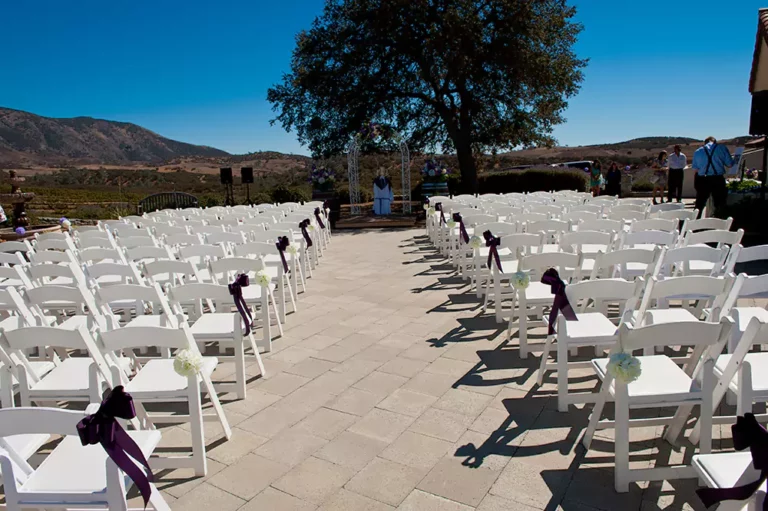 Outdoor wedding ceremony with white chairs and purple sashes at a beautiful wedding venue.