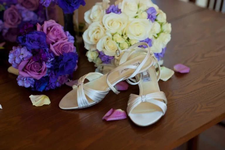 A pair of white shoes and a bouquet of purple and white roses.